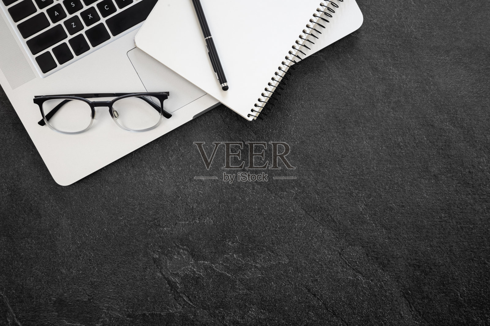 俯视图的笔记本电脑，眼镜和记事本在黑暗纹理的背景。照片摄影图片