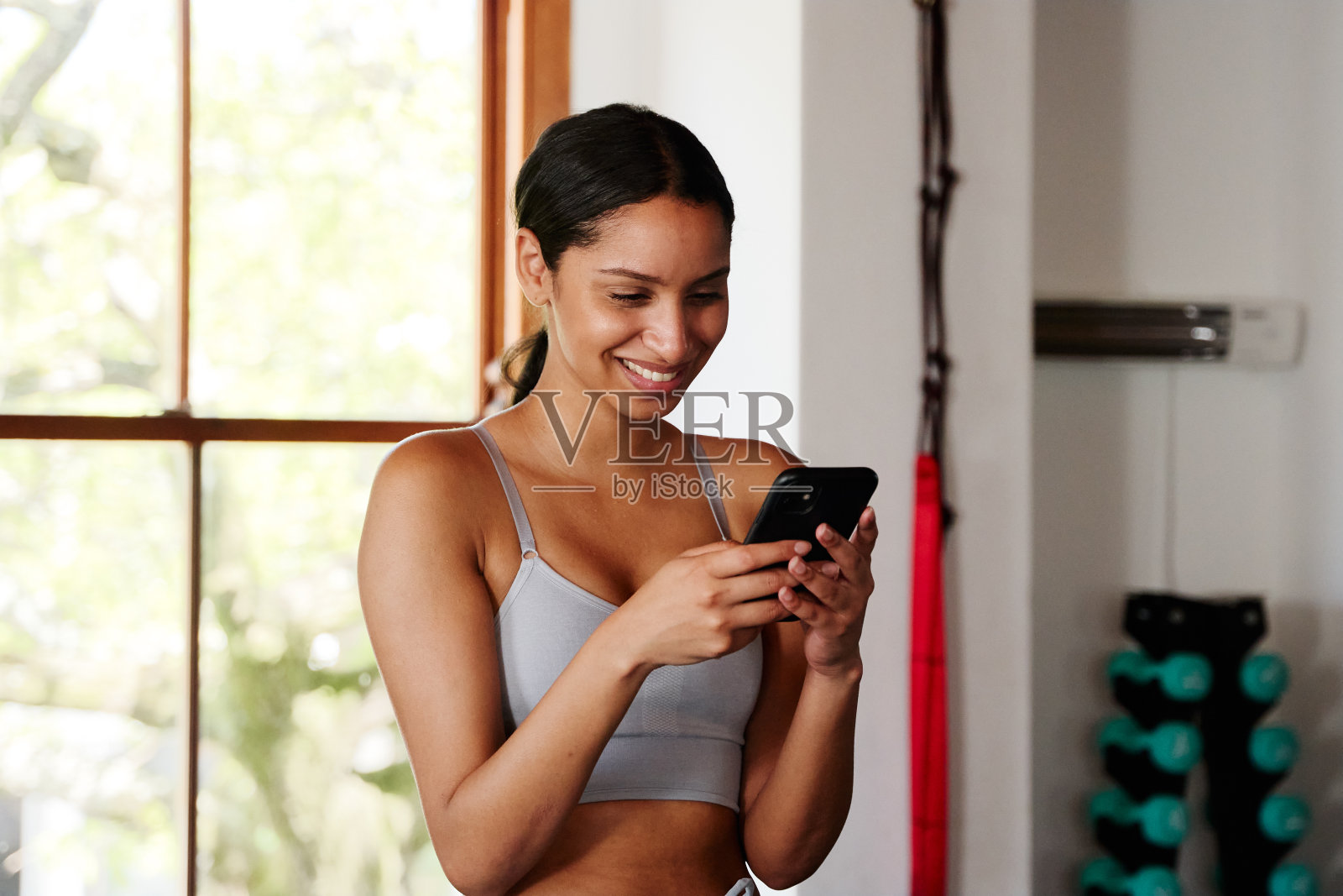 自信的年轻混血女人在健身房微笑着用手机打字照片摄影图片