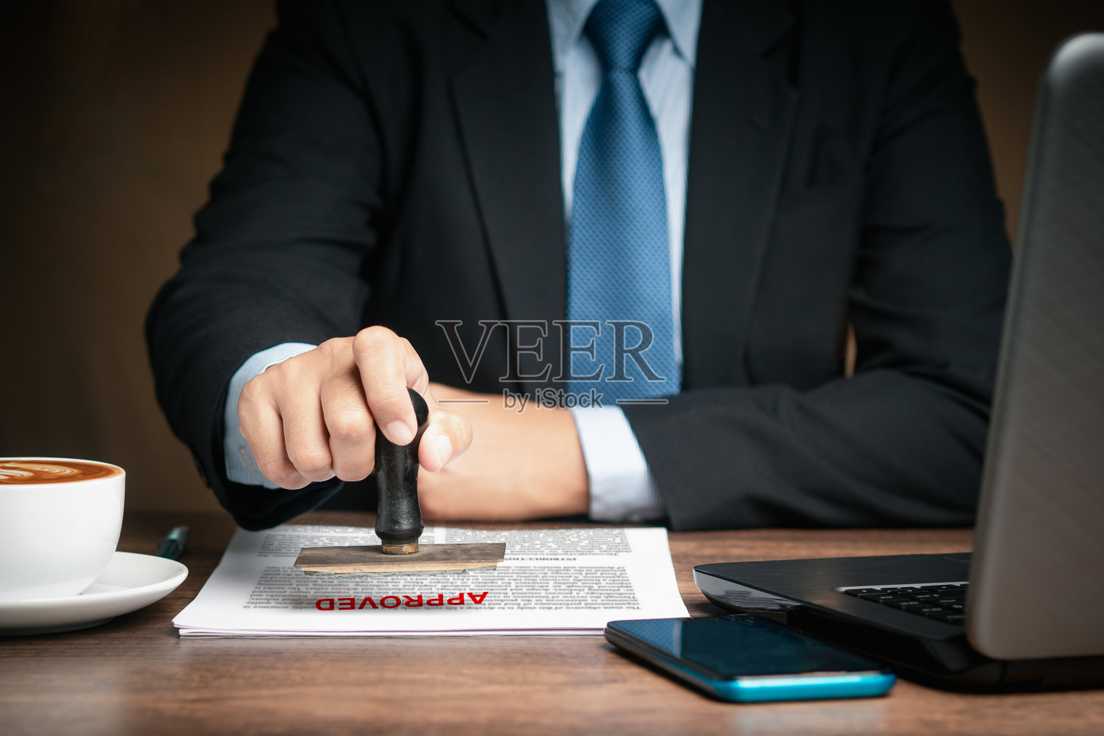 商人坐在办公室的桌子旁为批准的文件盖章照片摄影图片