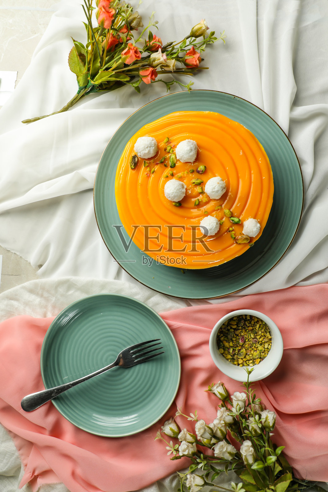 芒果酸奶蛋糕浇头与开心果叉子和鲜花服务于盘子孤立的餐巾顶视图咖啡馆烘焙食品照片摄影图片