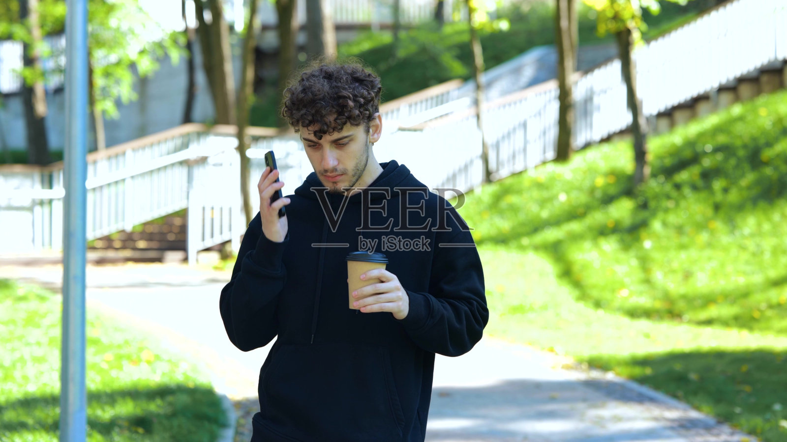 在公园里一边拿着咖啡一边咒骂尖叫的年轻人一边接手机电话。的生活方式。秋季散步的概念。慢动作照片摄影图片