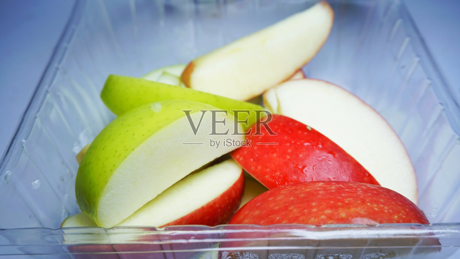 红的绿的苹果放在冰箱里的容器里。照片摄影图片