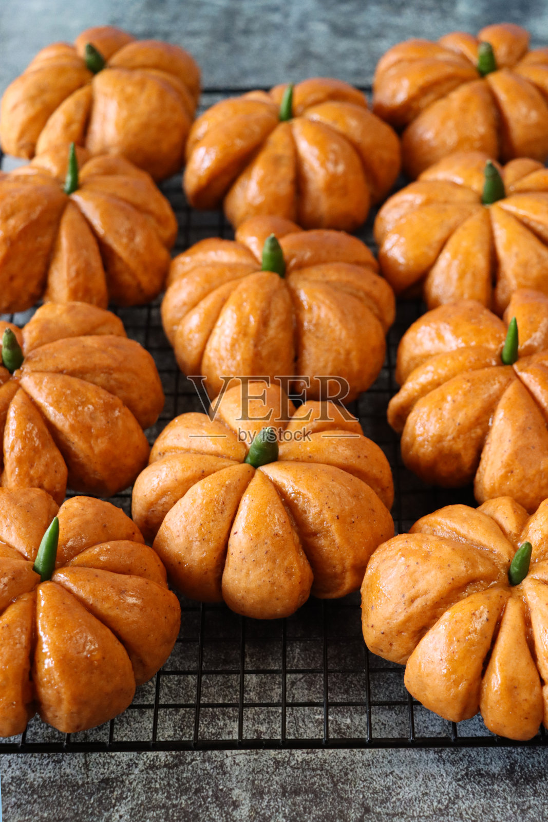 特写图片:成排新鲜出炉的自制万圣节南瓜卷，上面有绿辣椒梗，冷却架上涂着杏酱的面包，斑驳的灰色背景，高架视角，聚焦于前景照片摄影图片