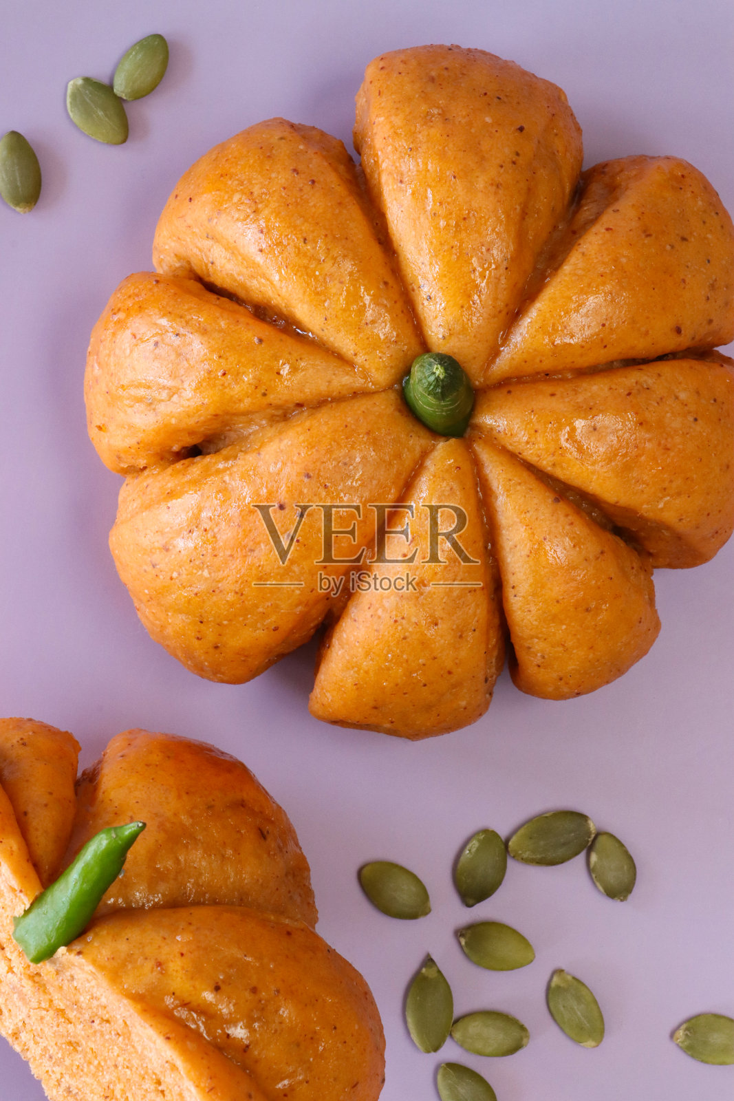 南瓜设计的南瓜卷的特写图片，绿色的辣椒茎被南瓜子包围，自制的万圣节面包包上涂着杏果酱，粉红色的背景，抬高的视图照片摄影图片