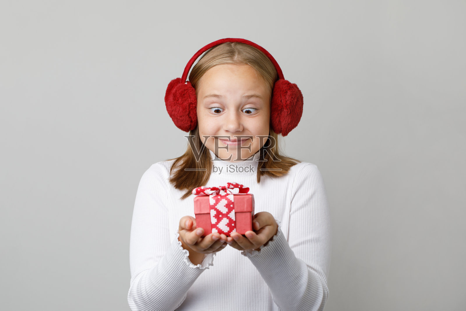 有趣而惊讶的小女孩看着红色的礼品盒，背景是白色的工作室墙壁横幅照片摄影图片