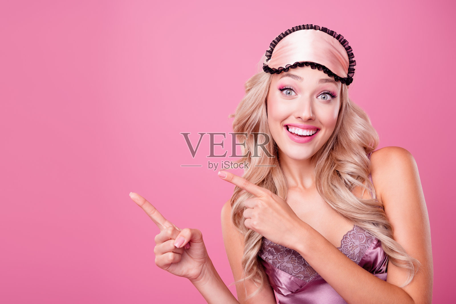 照片中兴高采烈的女士穿着丝绸睡衣，显示两根手指空白的空间孤立的粉红色背景照片摄影图片