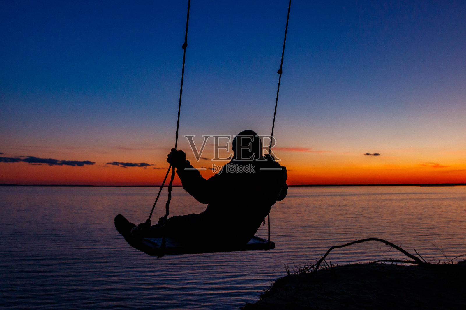 日落时分，一个人在河上荡秋千的剪影照片摄影图片