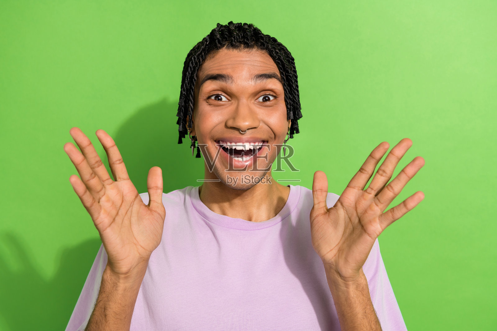 照片中，惊喜的年轻男子张开双手，手掌微笑，孤立在绿色的背景上照片摄影图片