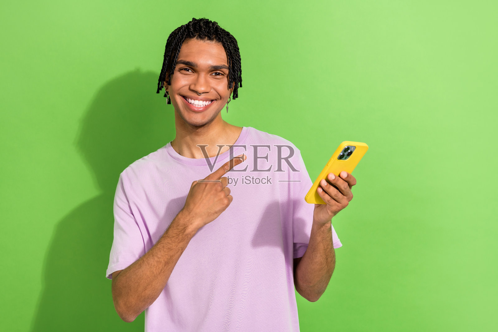 欢快的酷人的肖像，露齿微笑，手指，手臂，拿着苹果，iphone小工具，孤立在绿色的背景照片摄影图片