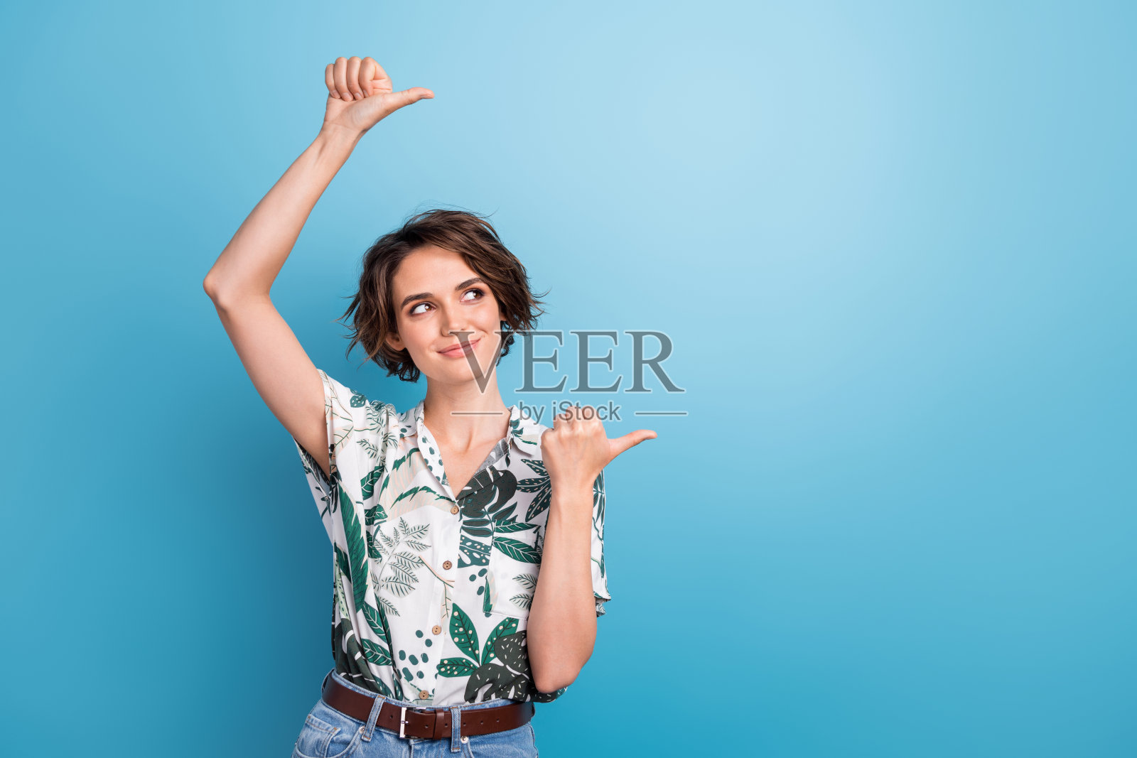 漂亮的年轻女孩的照片肖像，看着空白的空间，穿着时髦的印花叶子，在蓝色背景上孤立照片摄影图片