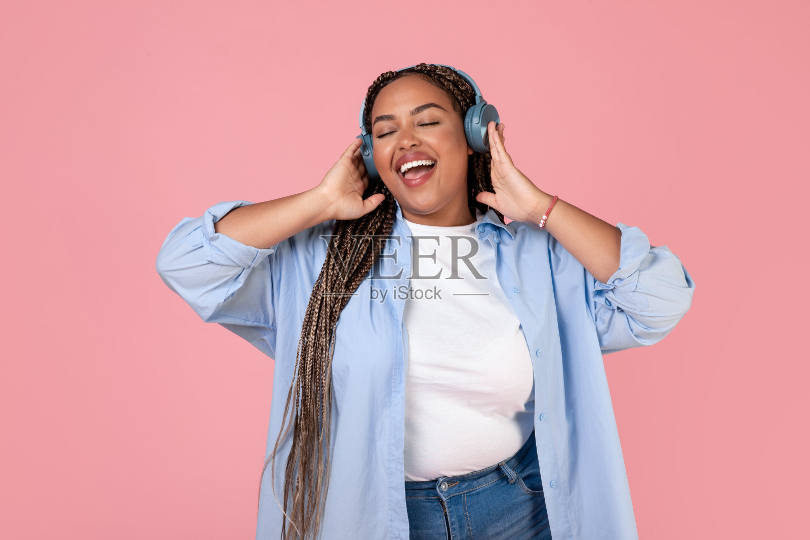 黑人女士戴着耳机在粉红色的背景下在线听音乐照片摄影图片