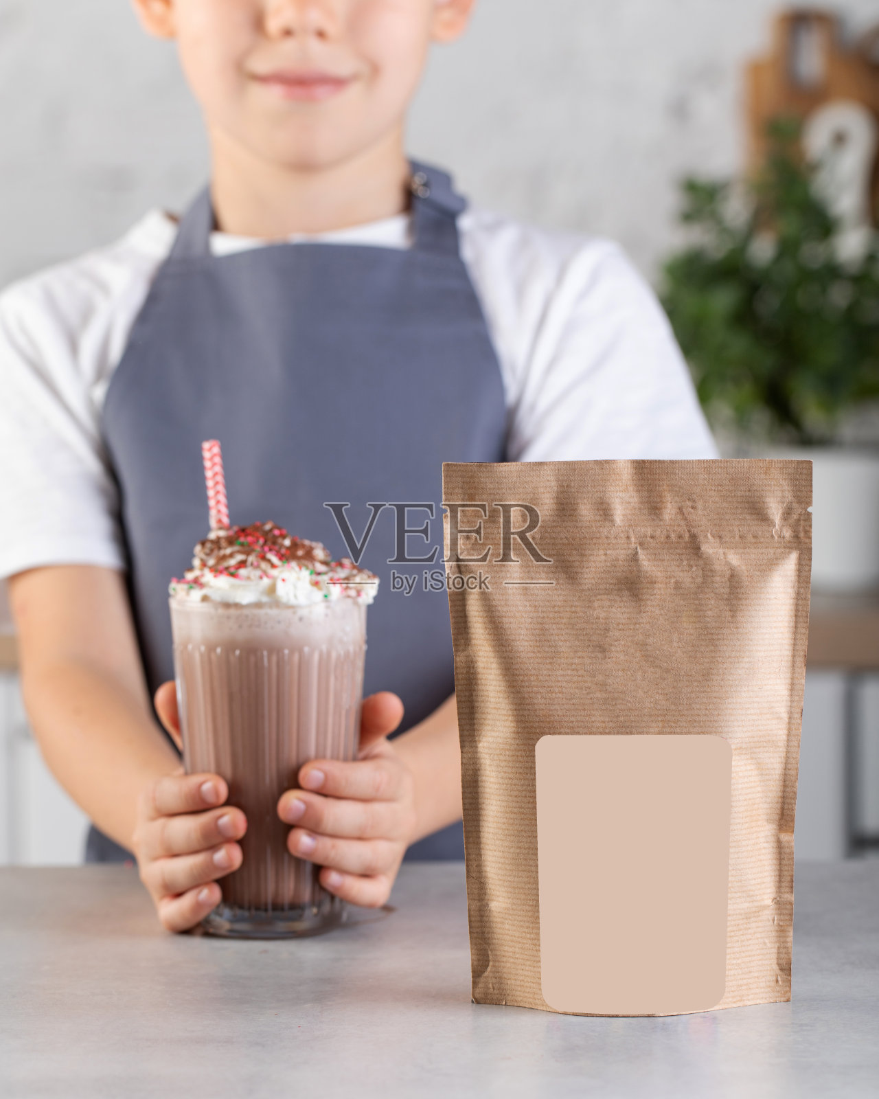 精心设计一个包装，在上面放上你的商标，还有一个可爱的男孩在厨房里拿着一杯巧克力奶昔。照片摄影图片