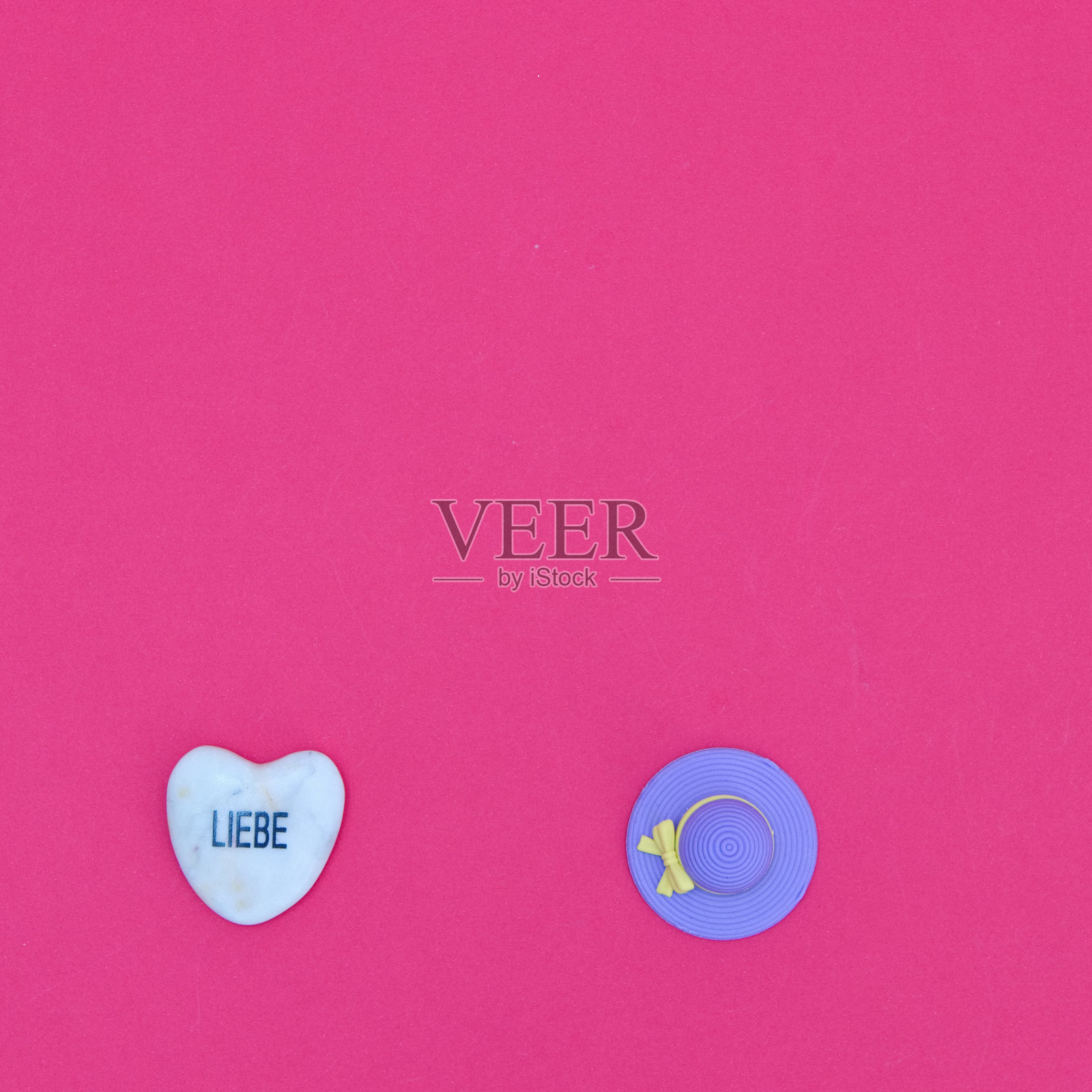 一块心形的石头，用德语写着“爱”，还有一顶红色背景的紫色沙滩帽。极简的平面与夏季的主题。照片摄影图片