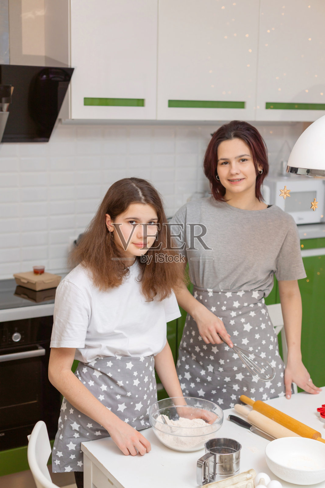 可爱的黑发姐妹十几岁的女孩在家里的餐桌上，在厨房里揉面团。为圣诞节制作饼干的过程。家庭的概念。照片摄影图片