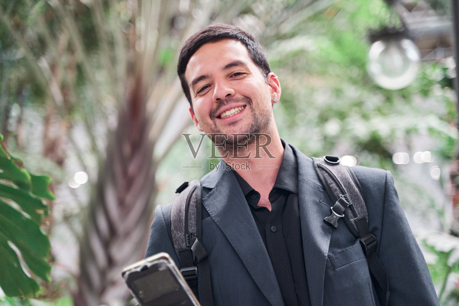 微笑的年轻拉丁裔男子在路上，手里拿着智能手机。照片摄影图片