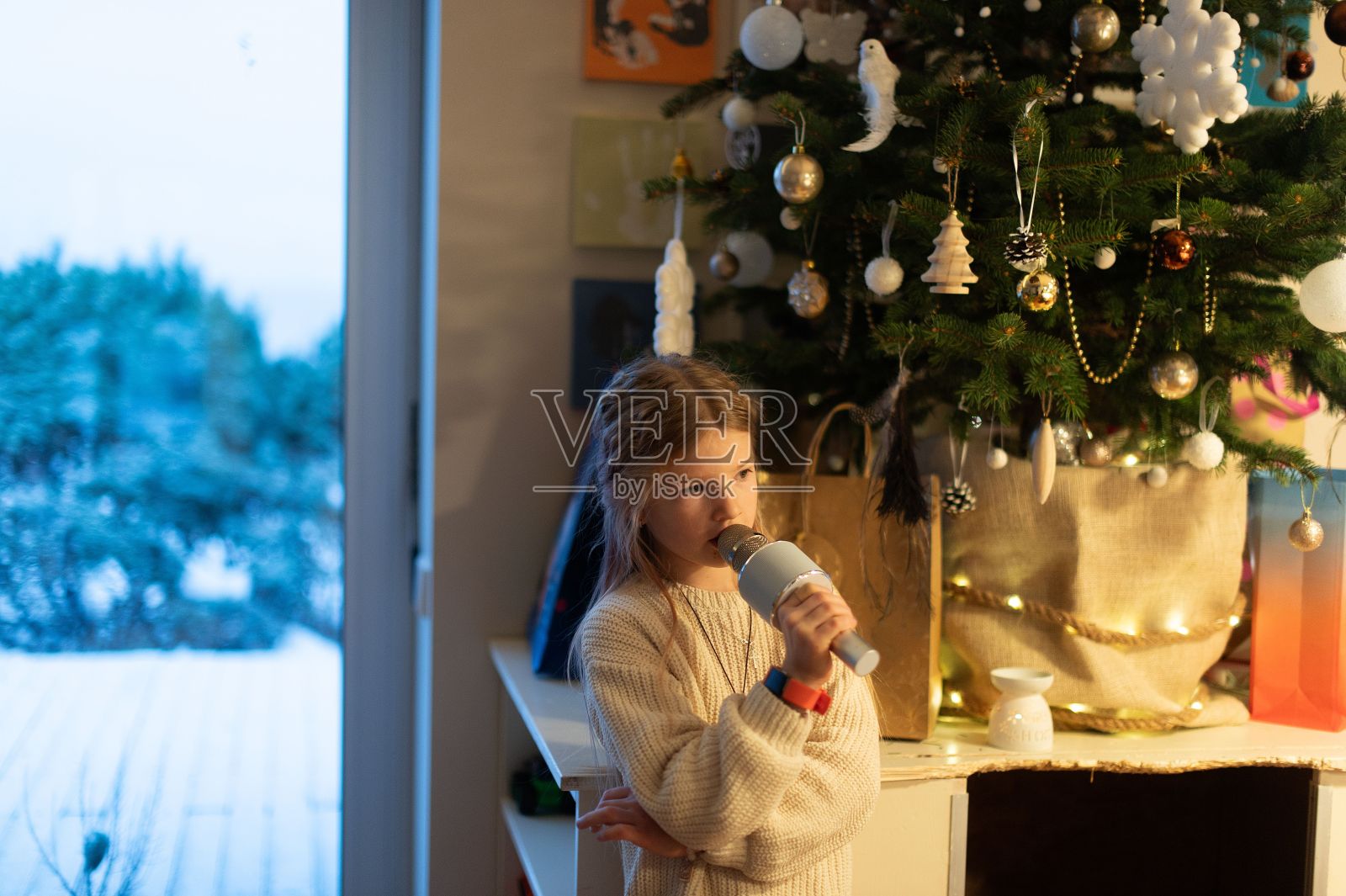 一个小女孩站在圣诞树旁边，圣诞树前面放着雪照片摄影图片