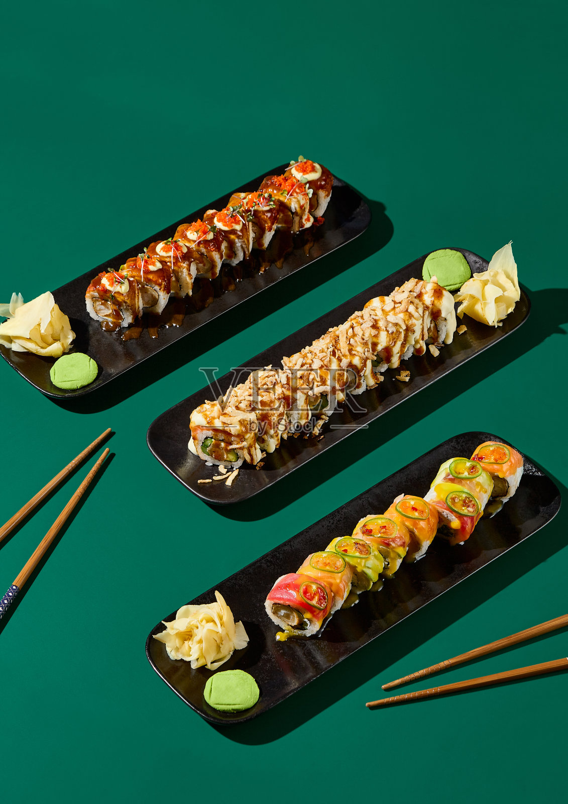 在深绿色的背景下，黑色的盘子里摆着一份寿司，引人注目的画面，筷子和坚硬的阴影。一个充满活力和现代极简主义组成的理想的亚洲餐厅菜单照片摄影图片