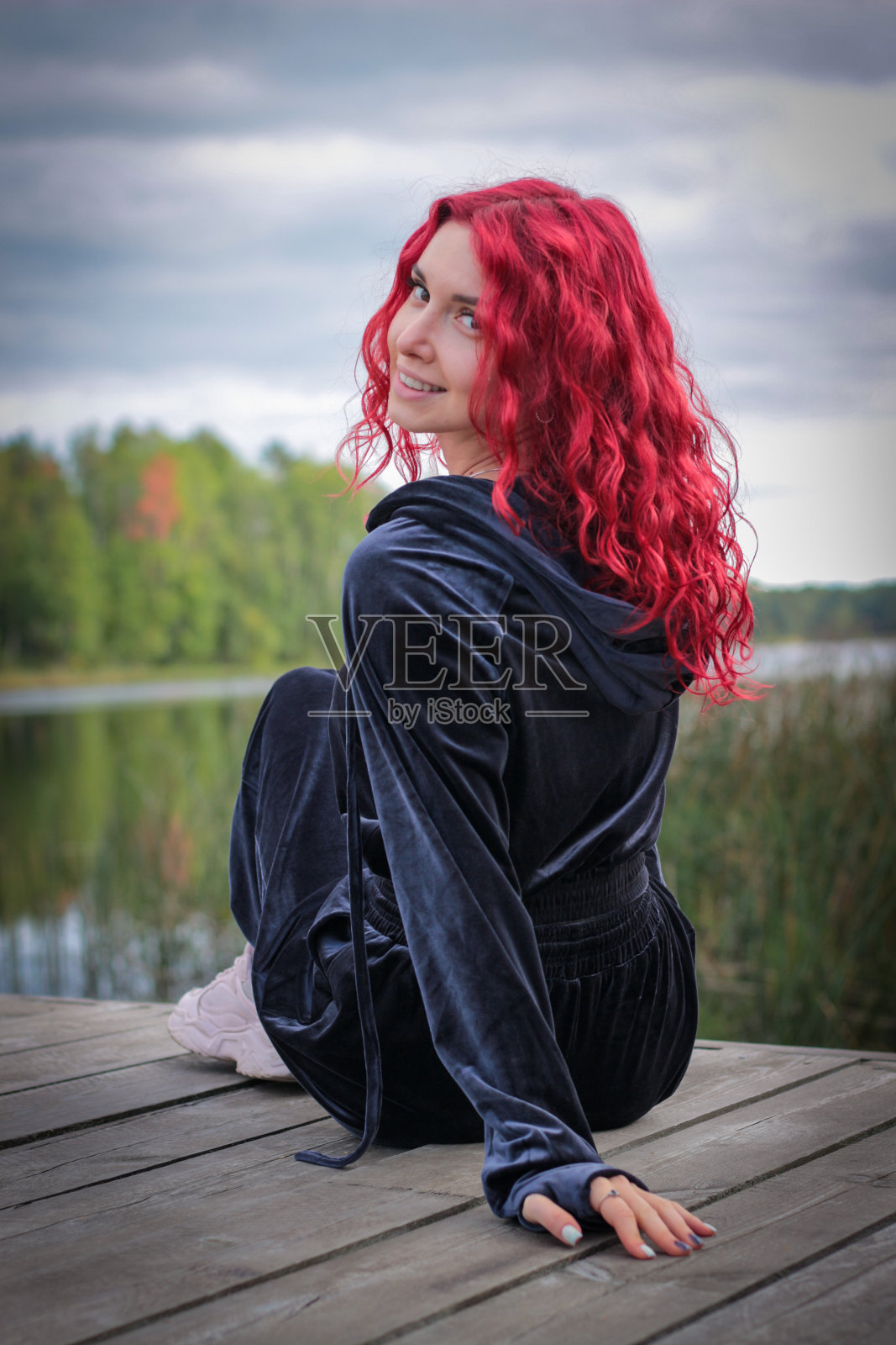 一个穿着运动服，红头发的时髦年轻女子站在河岸上的画像。照片摄影图片