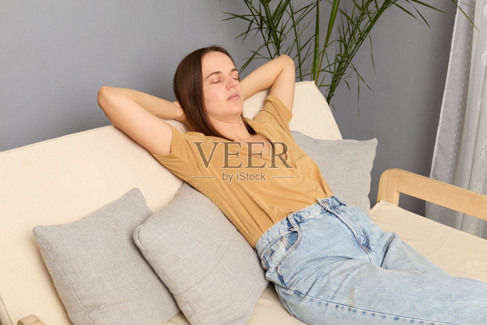 在现代的客厅里，年轻人坐在沙发上，双手放在脑后，在家里享受舒适的午睡，闭上眼睛，沉浸在梦中，花时间放松。照片摄影图片