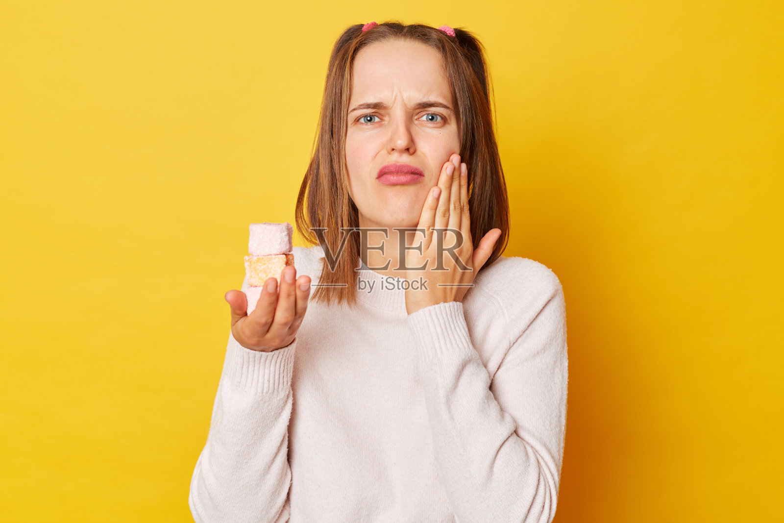 年轻漂亮的白人女子，马尾辫孤立在黄色背景上，因为吃了带糖的蛋糕，牙痛或牙病，用手摸着嘴，露出痛苦的表情。照片摄影图片