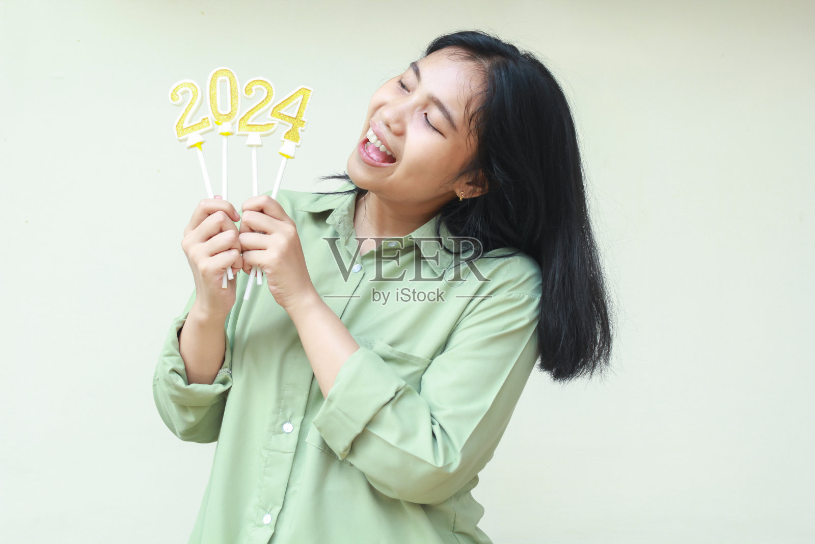 兴奋的亚洲年轻女子微笑着张开嘴，向旁边看2024年的数字蜡烛，手里拿着宣布2024年除夕，孤立的，女性穿着时尚的绿色大码衬衫照片摄影图片
