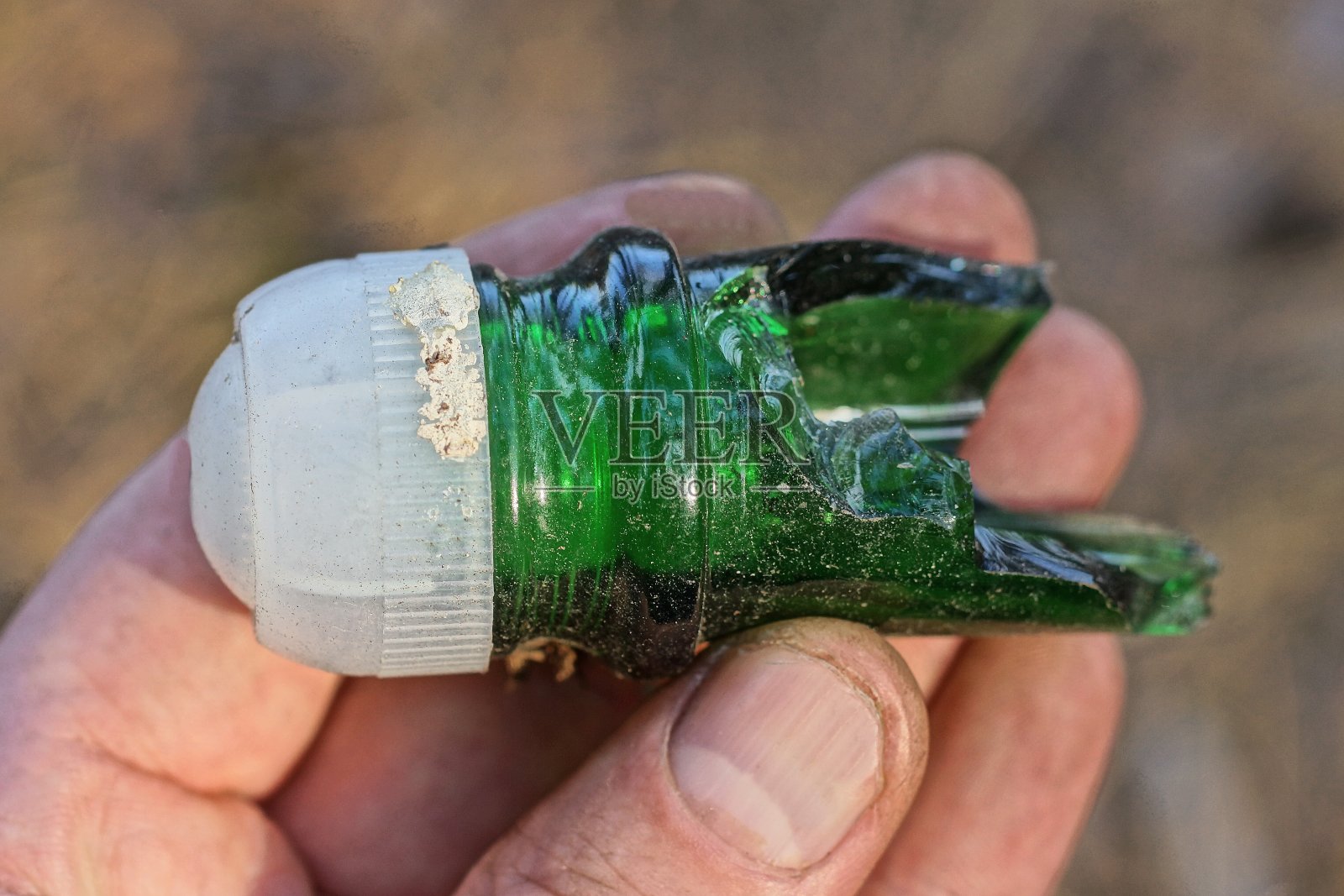 手里拿着一个旧玻璃，锋利的绿色脖子，一个破碎的白色塑料瓶塞照片摄影图片