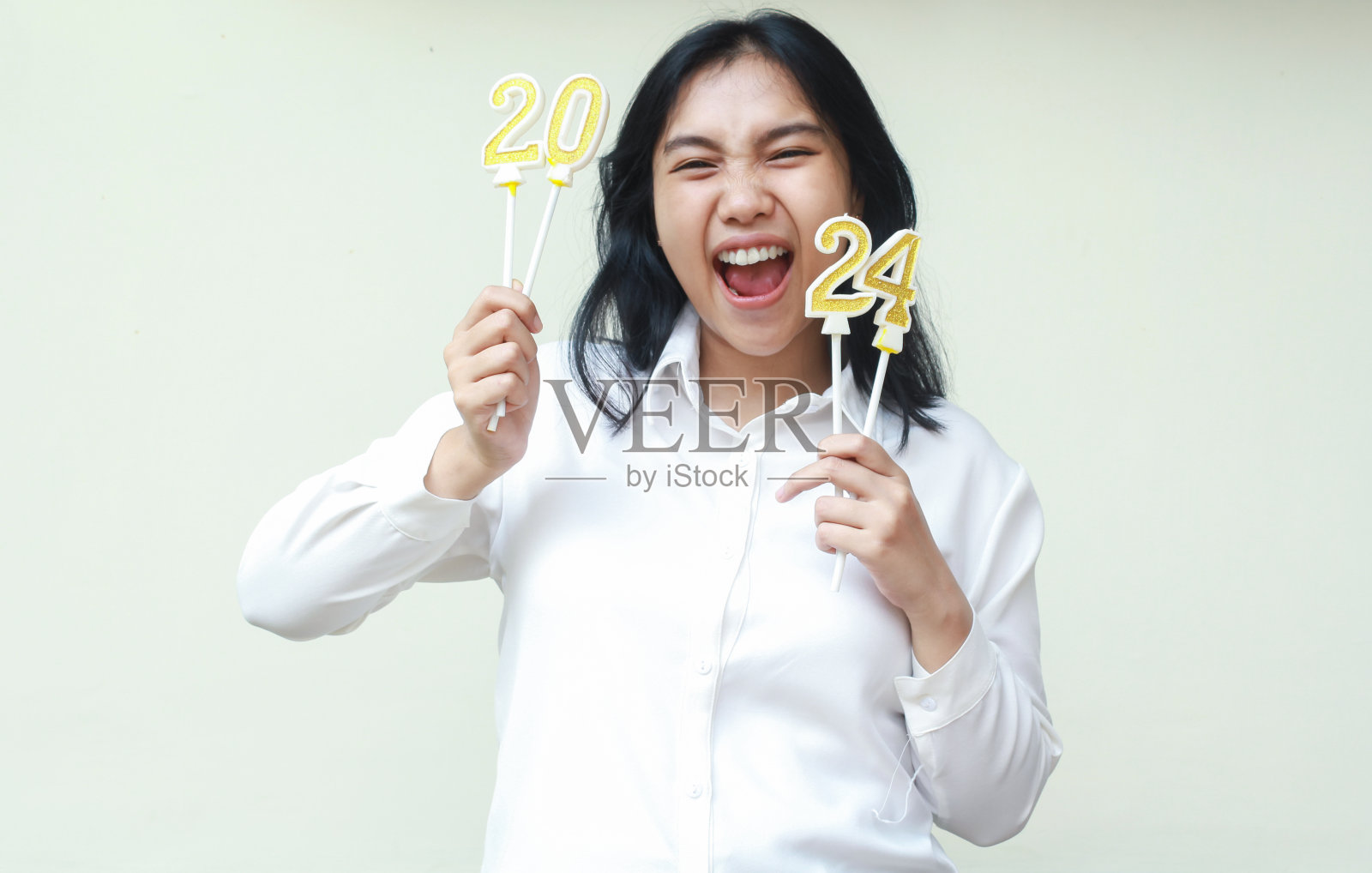 快乐的亚洲年轻女商人尖叫着举起手臂举着2024号蜡烛，孤独的女同事穿着白色正装庆祝新年照片摄影图片