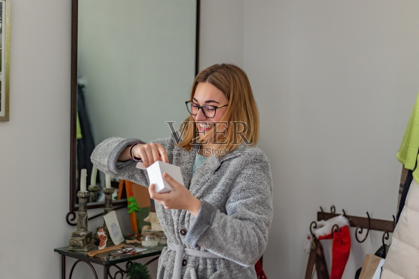 戴着眼镜的年轻金发女子在圣诞节早晨急切地拆开礼物。照片摄影图片
