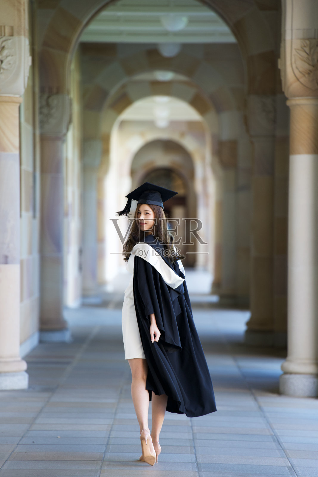 快乐的年轻女子在大学校园户外拍摄肖像，穿着毕业礼服，庆祝学业成就的亚洲美丽国际学生照片摄影图片