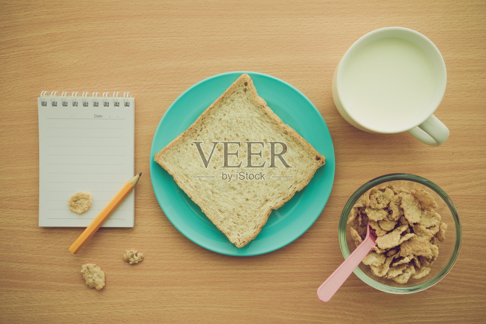 把全麦面包放在盘子里，牛奶，早餐麦片和空白的笔记本放在木桌背景上。照片摄影图片