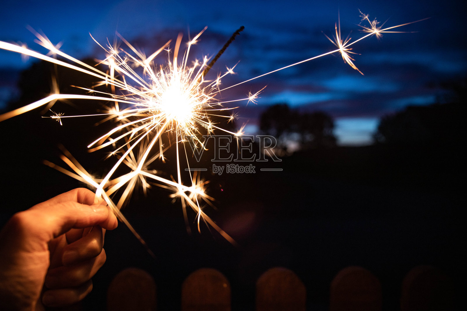 在蓝色的时刻，手握着燃烧的火花。照片摄影图片