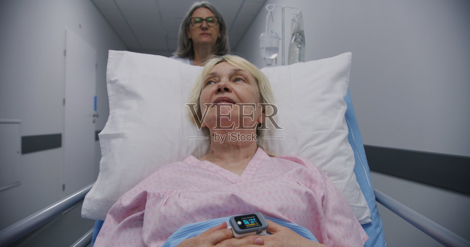 老妇人躺在打点滴的轮床上和医护人员交谈照片摄影图片