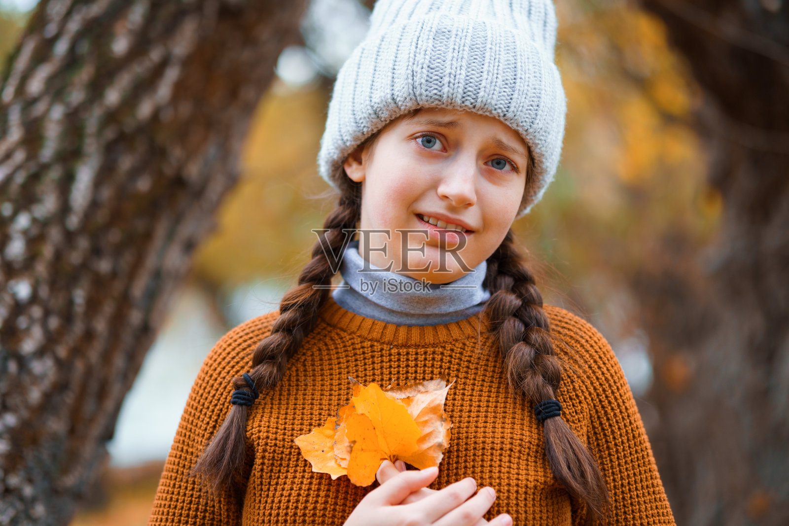一个十几岁的女孩在秋天的森林里摆姿势，站在河边的一棵树旁，享受着美丽的大自然和明亮的黄色树叶照片摄影图片