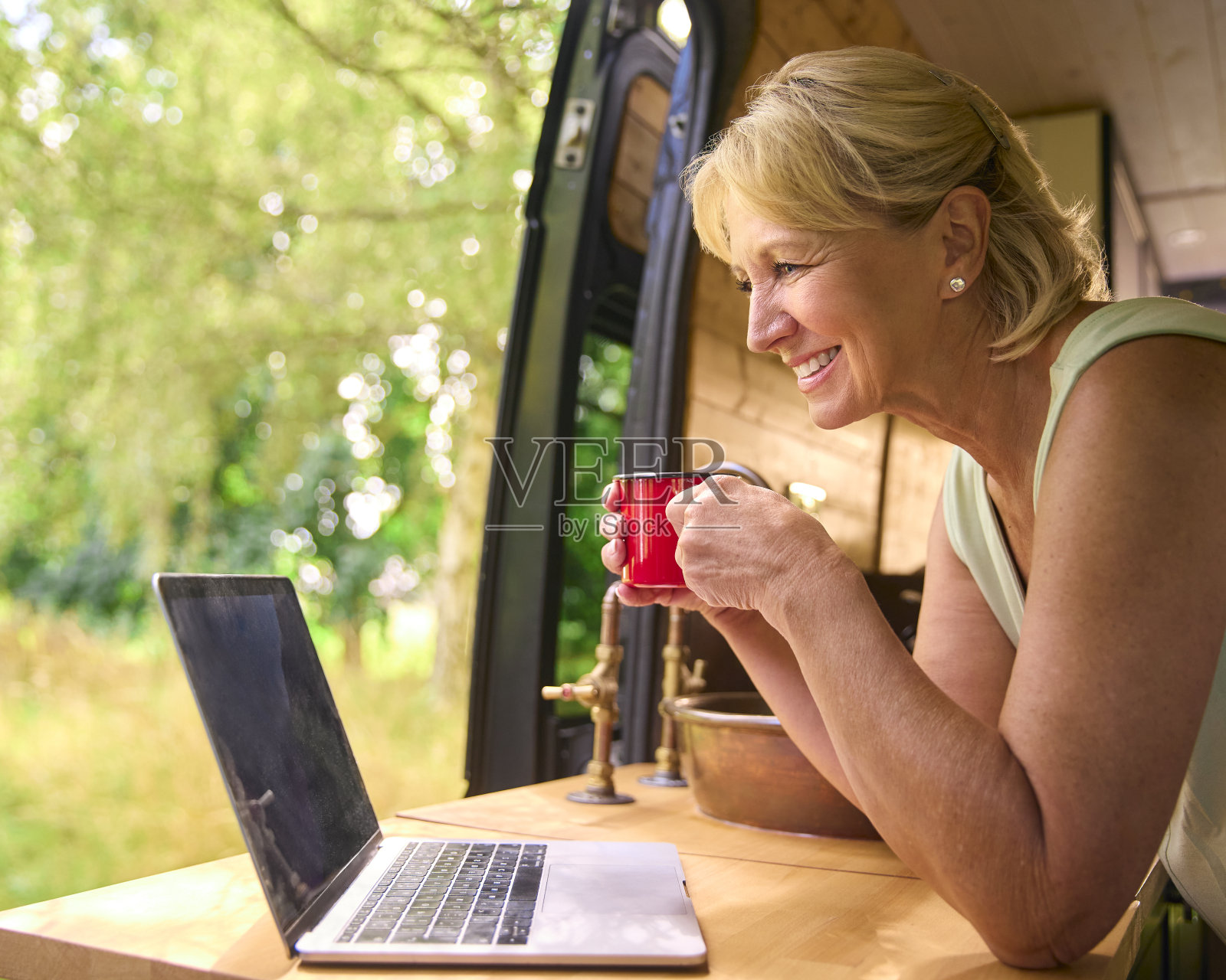 在农村露营旅行的老年妇女使用笔记本电脑在房车内工作照片摄影图片