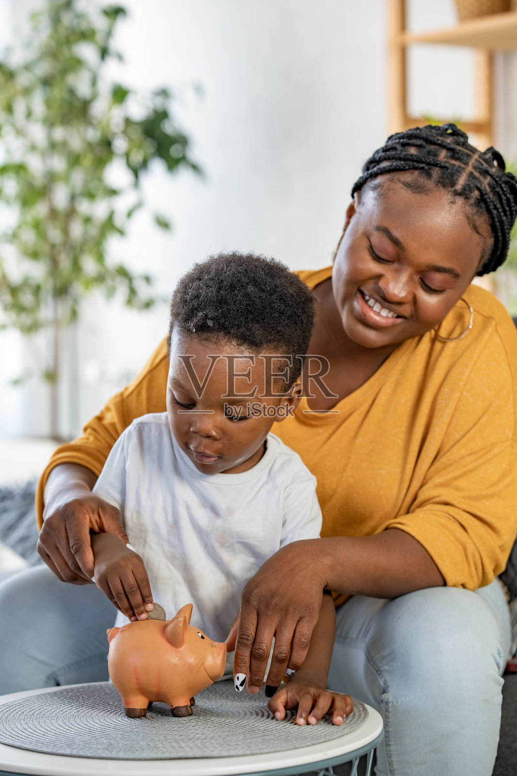 可爱的非裔美国小男孩和他的妈妈把一枚硬币放进储蓄罐，金融和银行的概念照片摄影图片