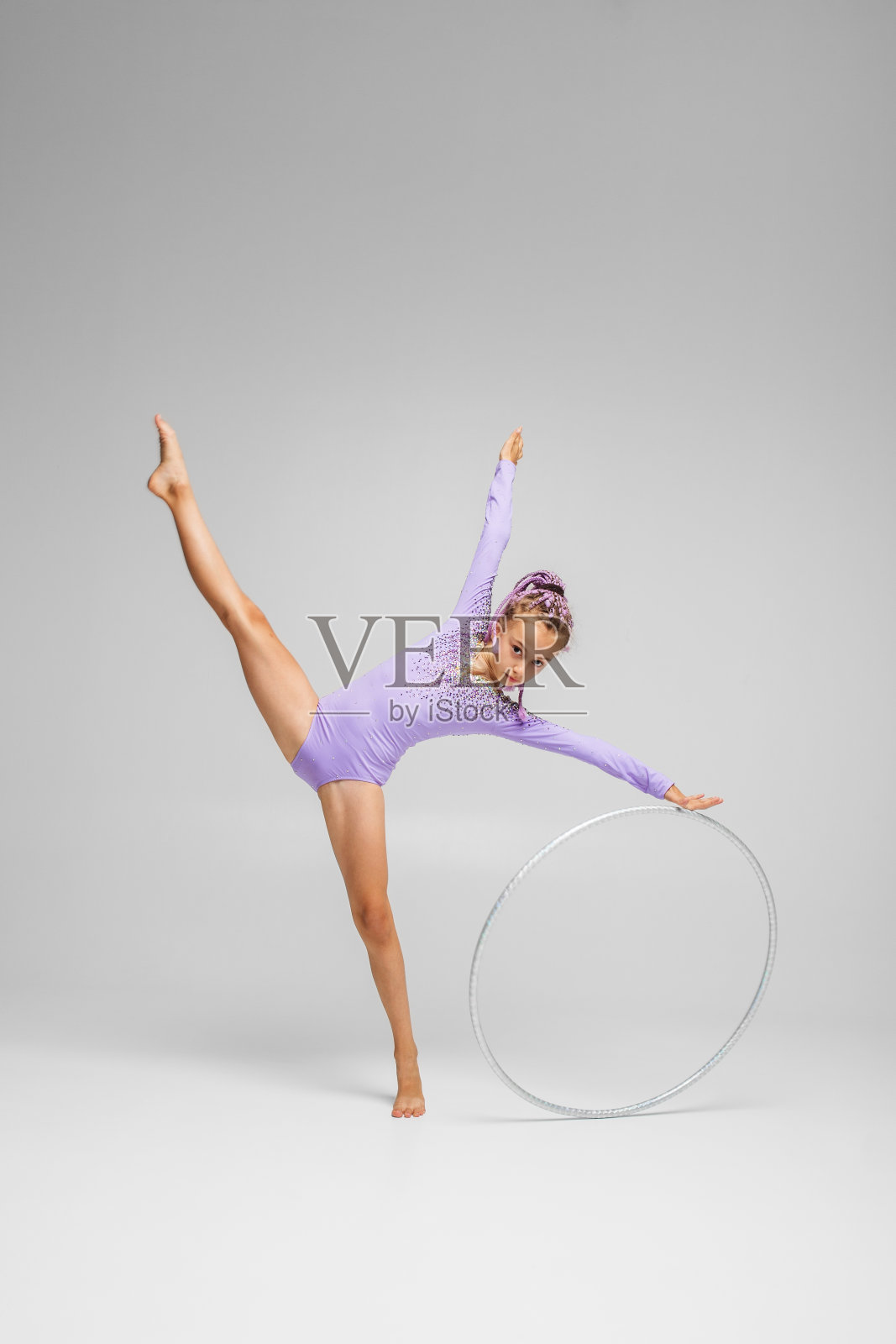 艺术体操。体操女孩穿着紫色的泳装做着带箍的运动。照片摄影图片