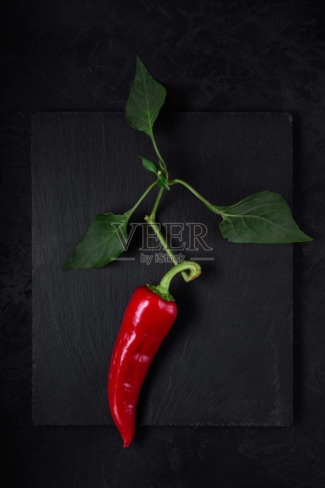一根带叶子的树枝上的红辣椒躺在黑色的石头砧板上。从上面看。简单的艺术暗照片照片摄影图片