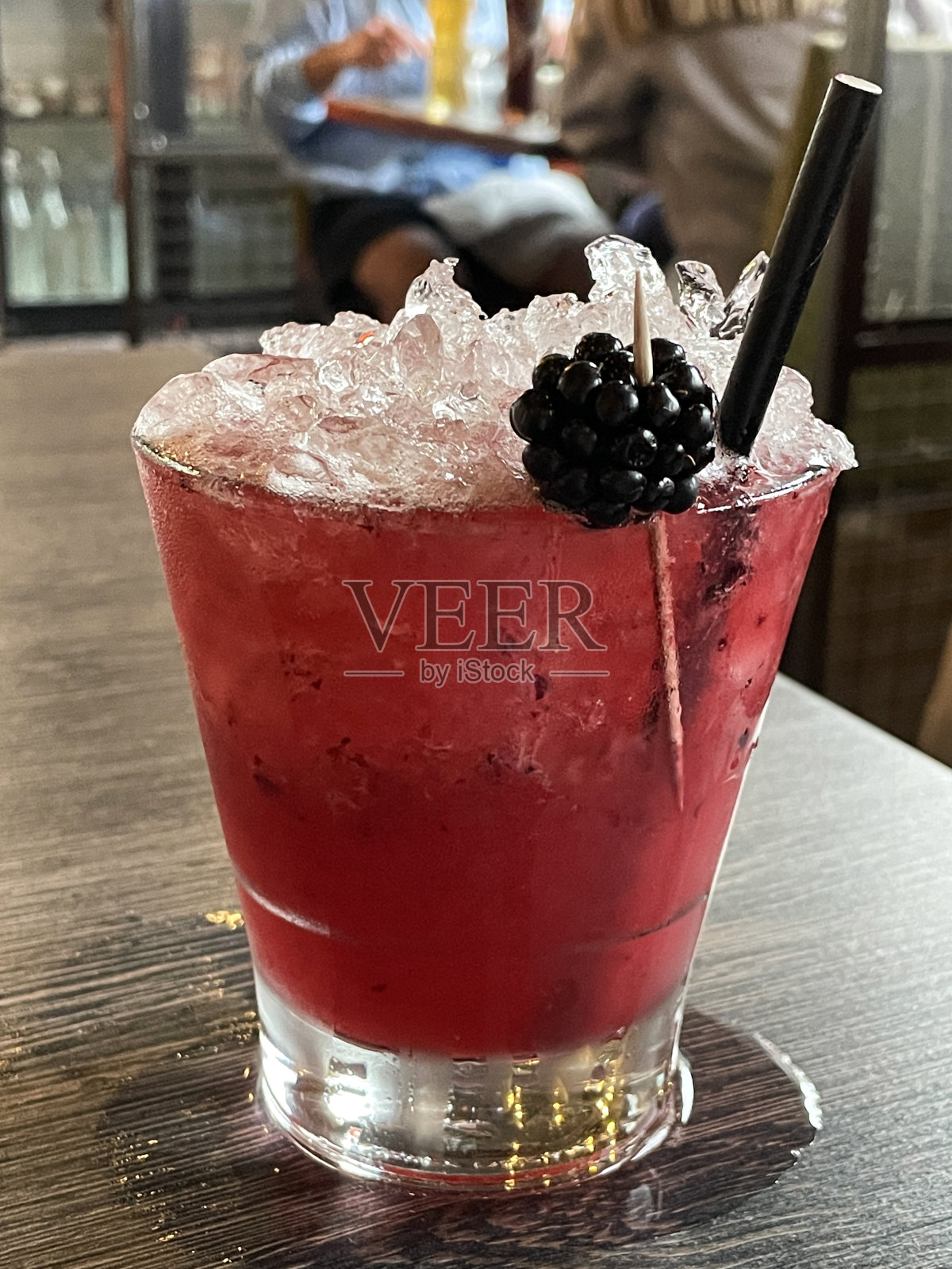 酒吧设置的特写图片，喝一杯加冰的黑莓鸡尾酒，黑莓鸡尾酒棒和黑纸吸管，桌子，焦点在前景照片摄影图片