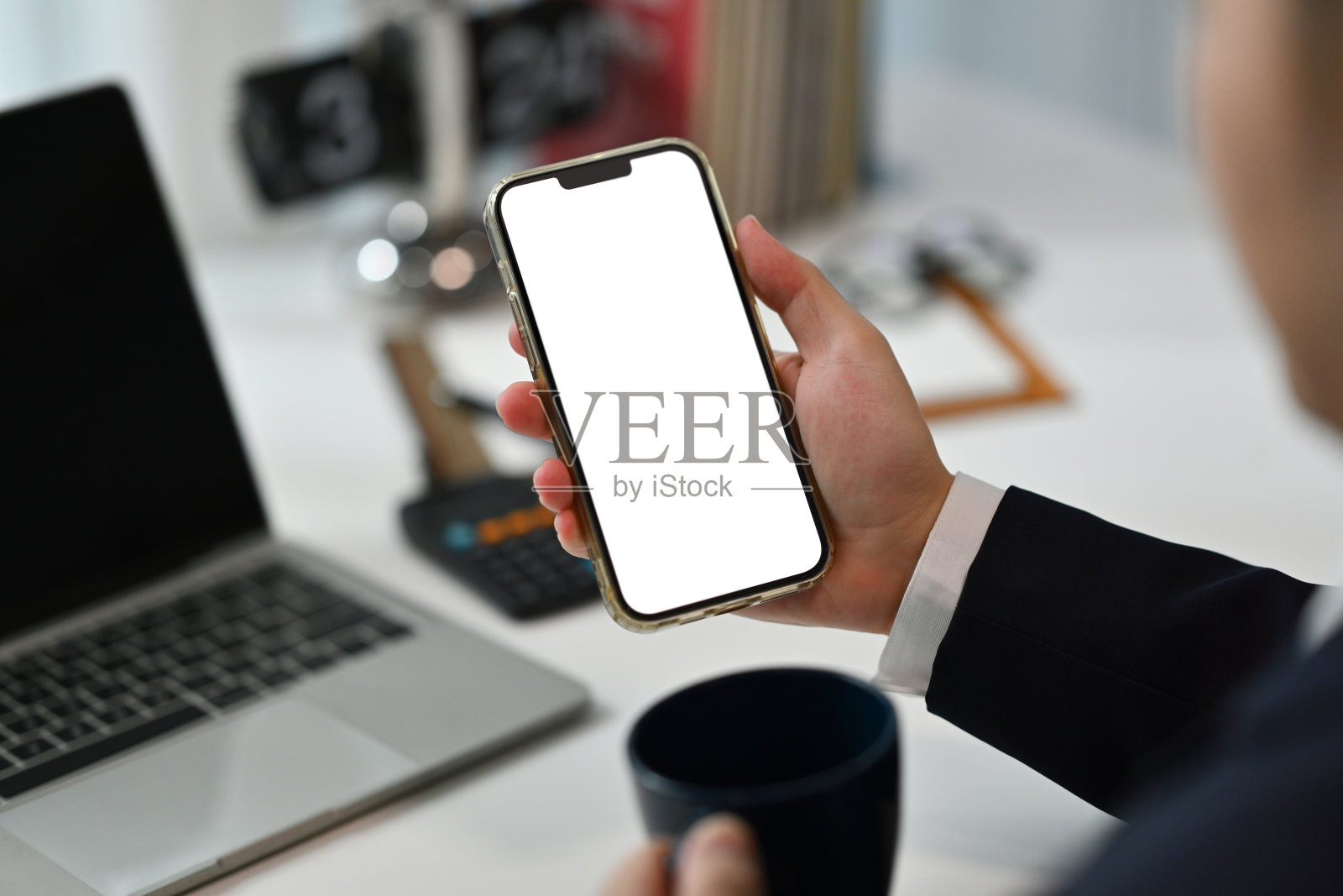 从肩膀上看商人拿着咖啡杯咖啡，在办公桌上使用智能手机照片摄影图片