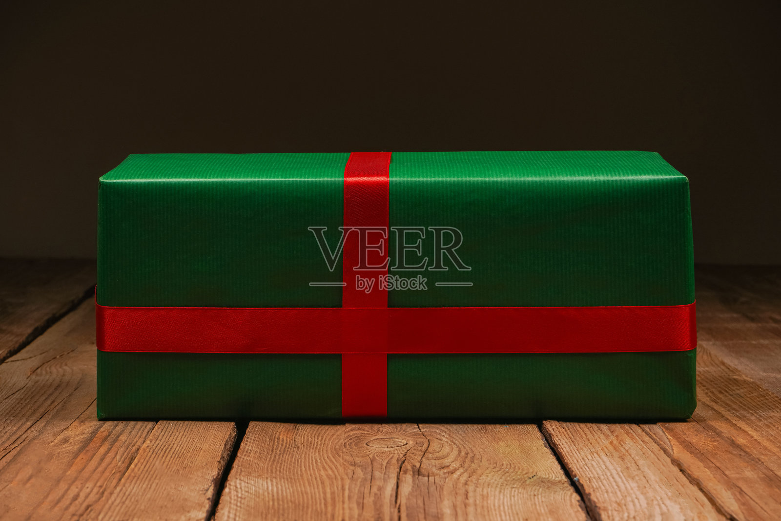 节日绿色礼盒与红色缎面蝴蝶结，丝带。手工木制背景上的礼物。情人节，妇女节，母亲节，生日，婚礼，圣诞节。照片摄影图片