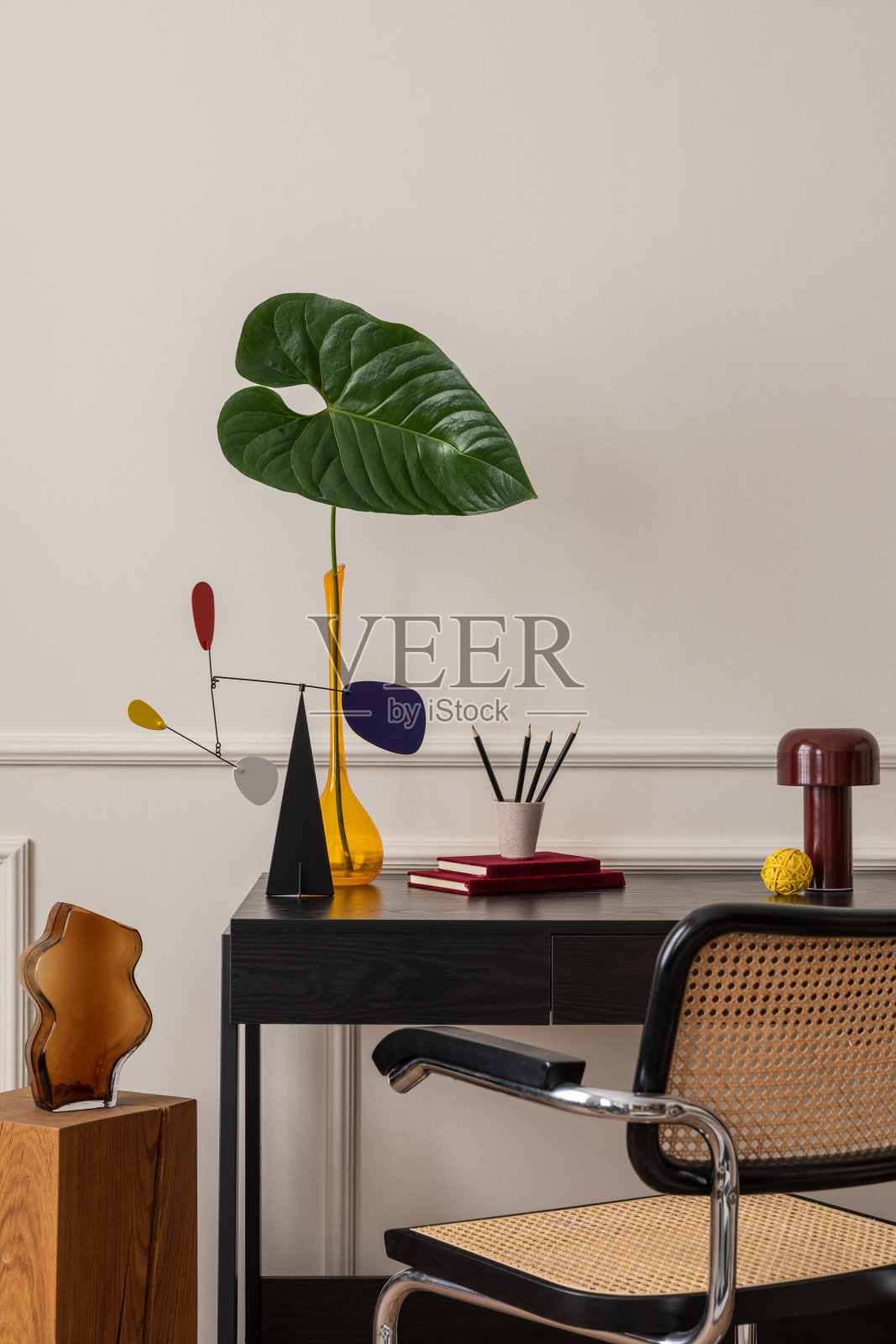 黑色办公桌，藤椅，彩色雕塑，树叶花瓶，架子，书籍，粉刷墙和个人配件的现代职场室内构成。家居装饰。模板。照片摄影图片