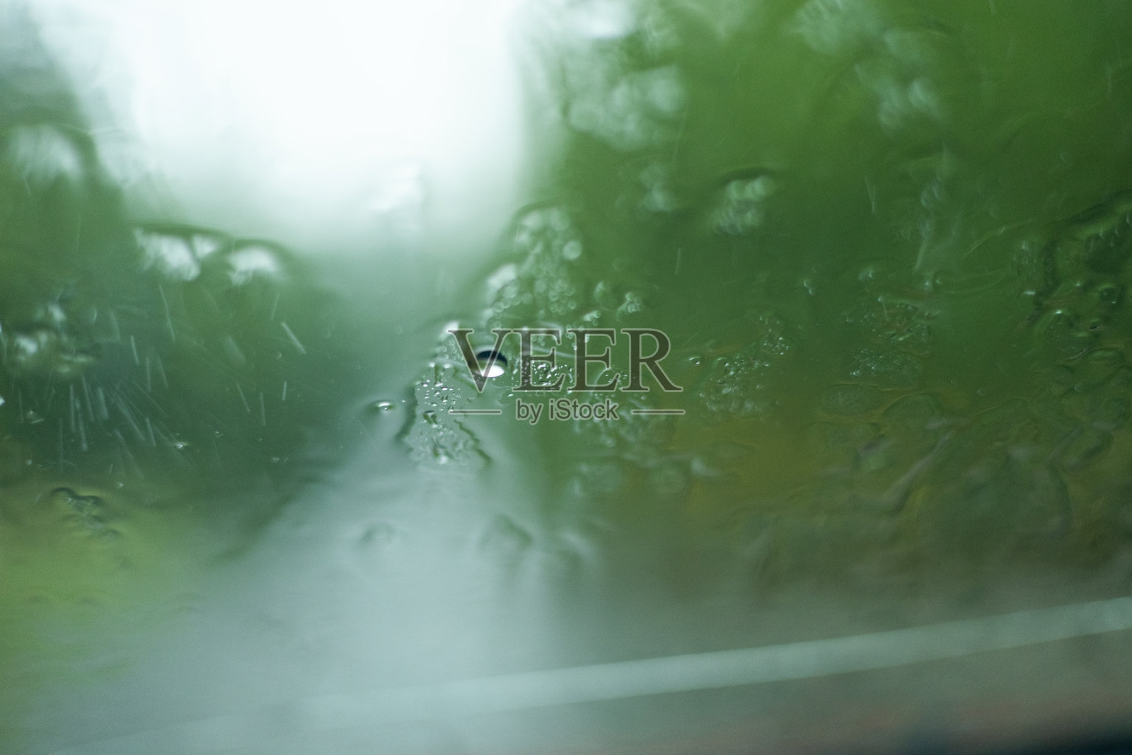 大雨时雨点顺着汽车的挡风玻璃流下来。雨滴落在车窗上的特写镜头。下雨时，水珠顺着玻璃流下来。照片摄影图片