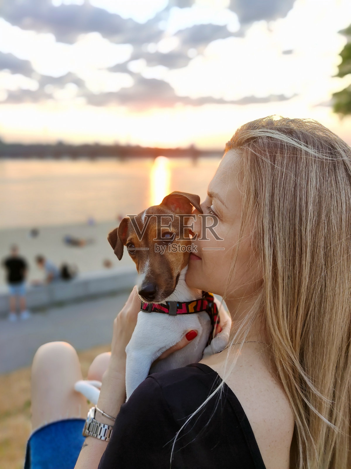 一个年轻漂亮的女人坐在河边，怀里抱着一只杰克罗素梗狗，面带微笑照片摄影图片