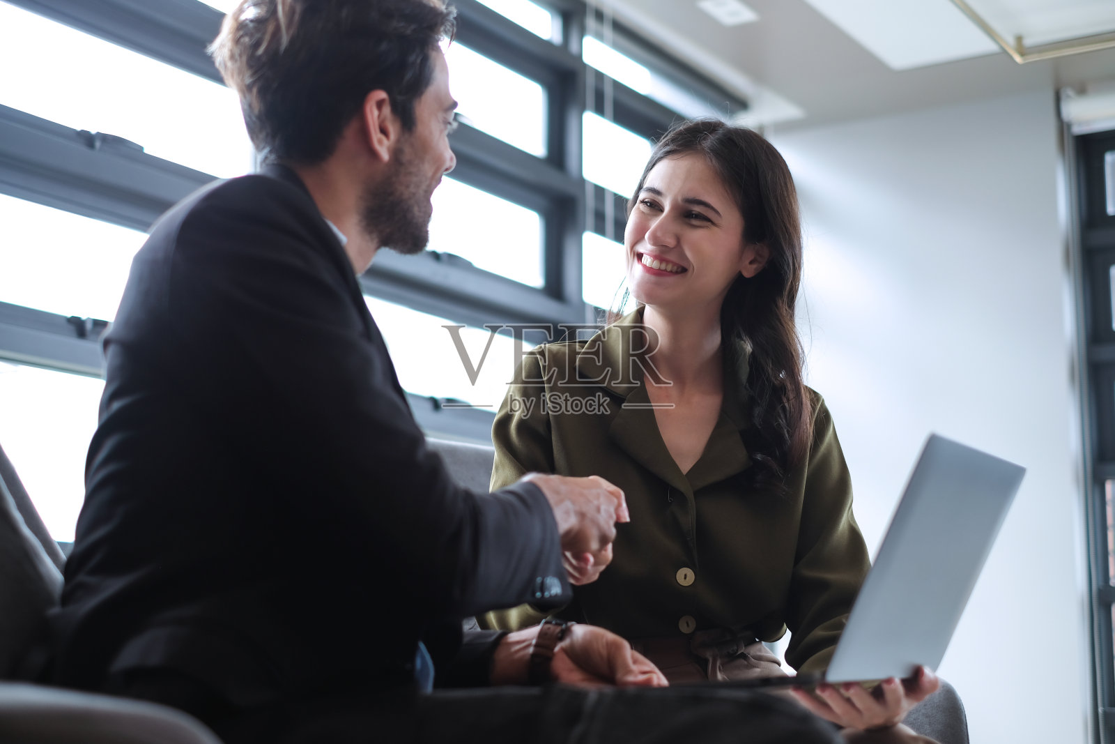 自信的年轻女商人与白人商人握手，祝贺商业伙伴成功就职。照片摄影图片