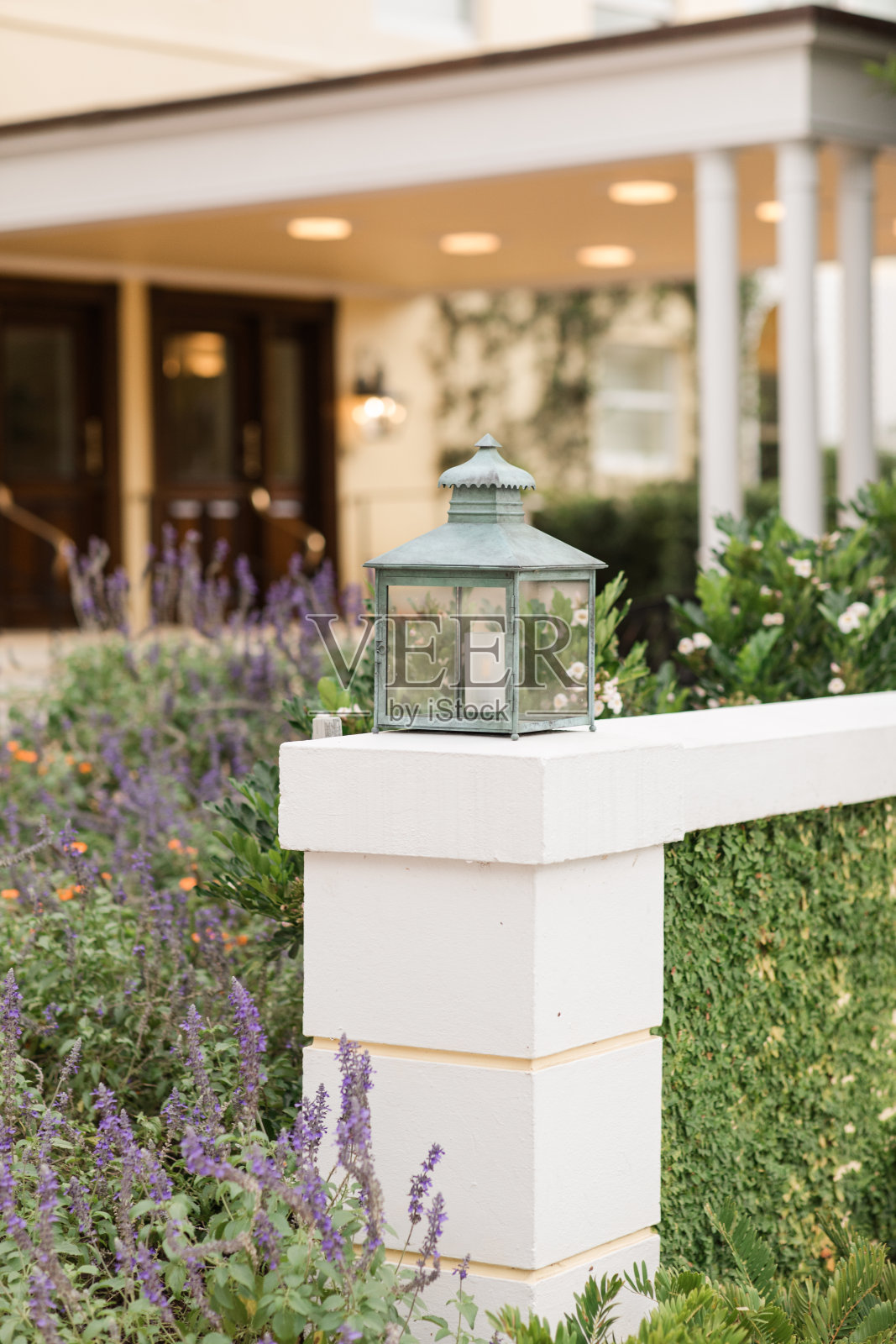 在佛罗里达州棕榈滩，被紫色和橙色的花朵和绿色环绕的室外混凝土墙上挂着质朴的蓝绿色灯笼照片摄影图片