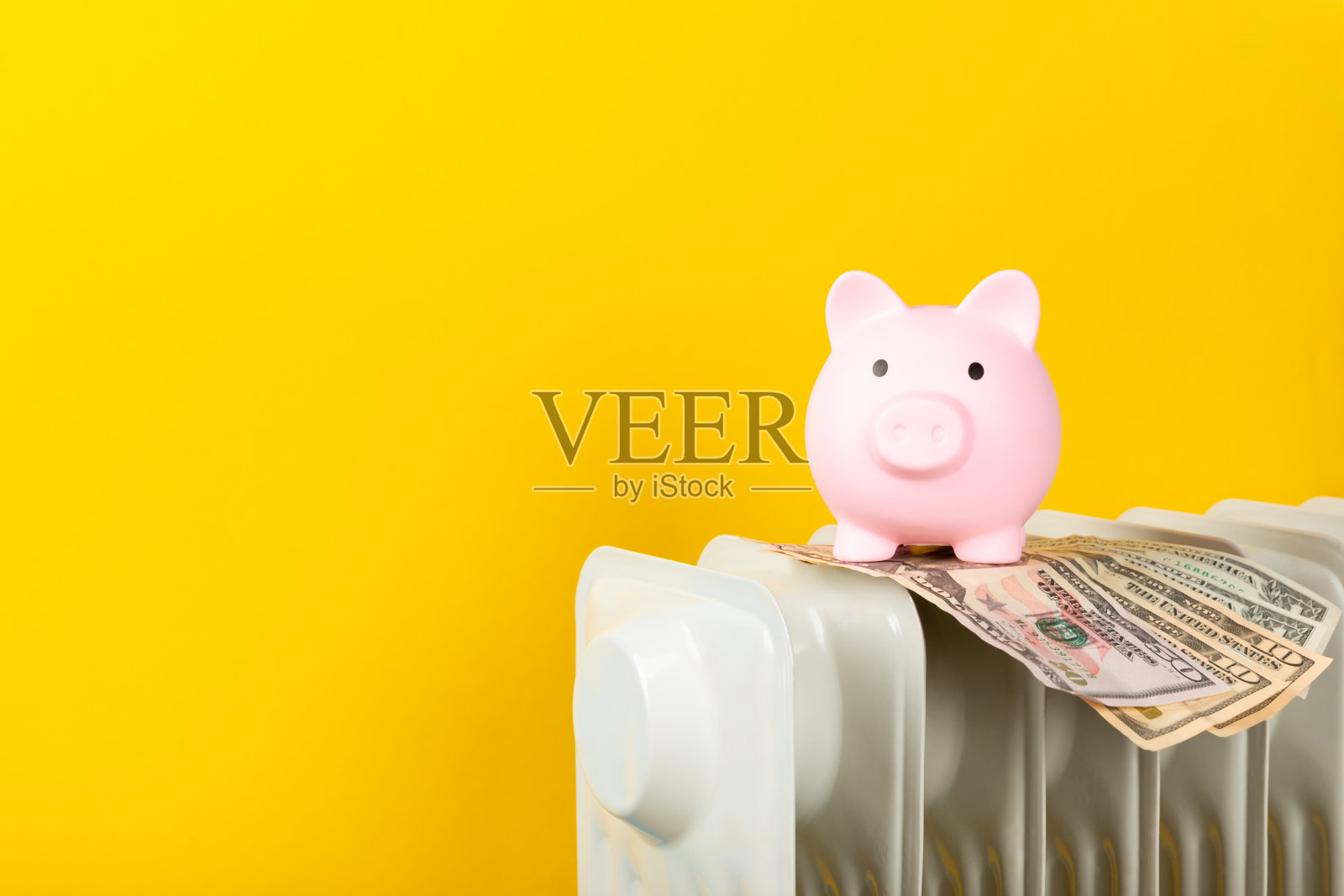 储蓄的概念。黄墙背景上暖气片上存钱罐里的钱。供暖季节的概念。冬季寒冷季节昂贵的取暖费用和能源账单价格上涨的概念。照片摄影图片