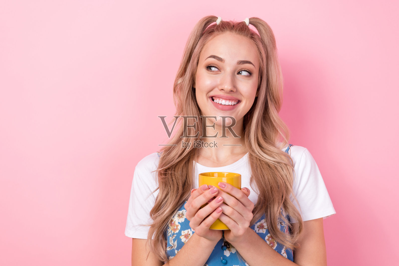 照片中可爱可爱的女人穿着花印花整体拿着一杯咖啡看起来空白的空间孤立在粉红色的背景照片摄影图片