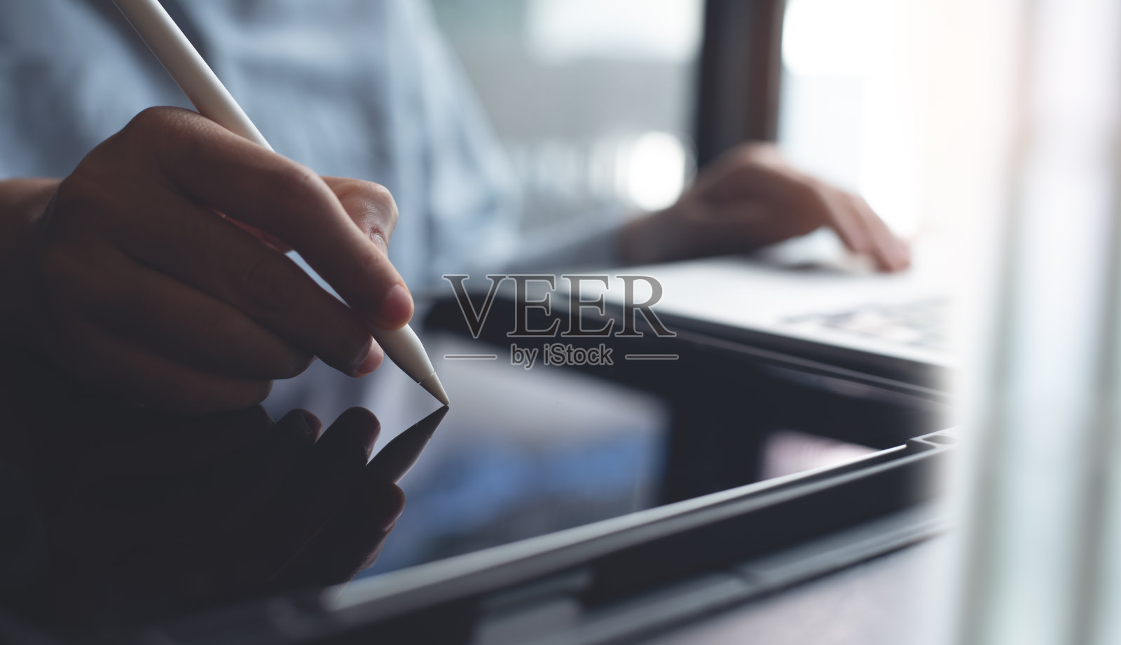 商务女性在办公室用笔记本电脑工作时，用电子笔触摸平板电脑屏幕的特写。电子文件打样，电子签名，电子签名照片摄影图片