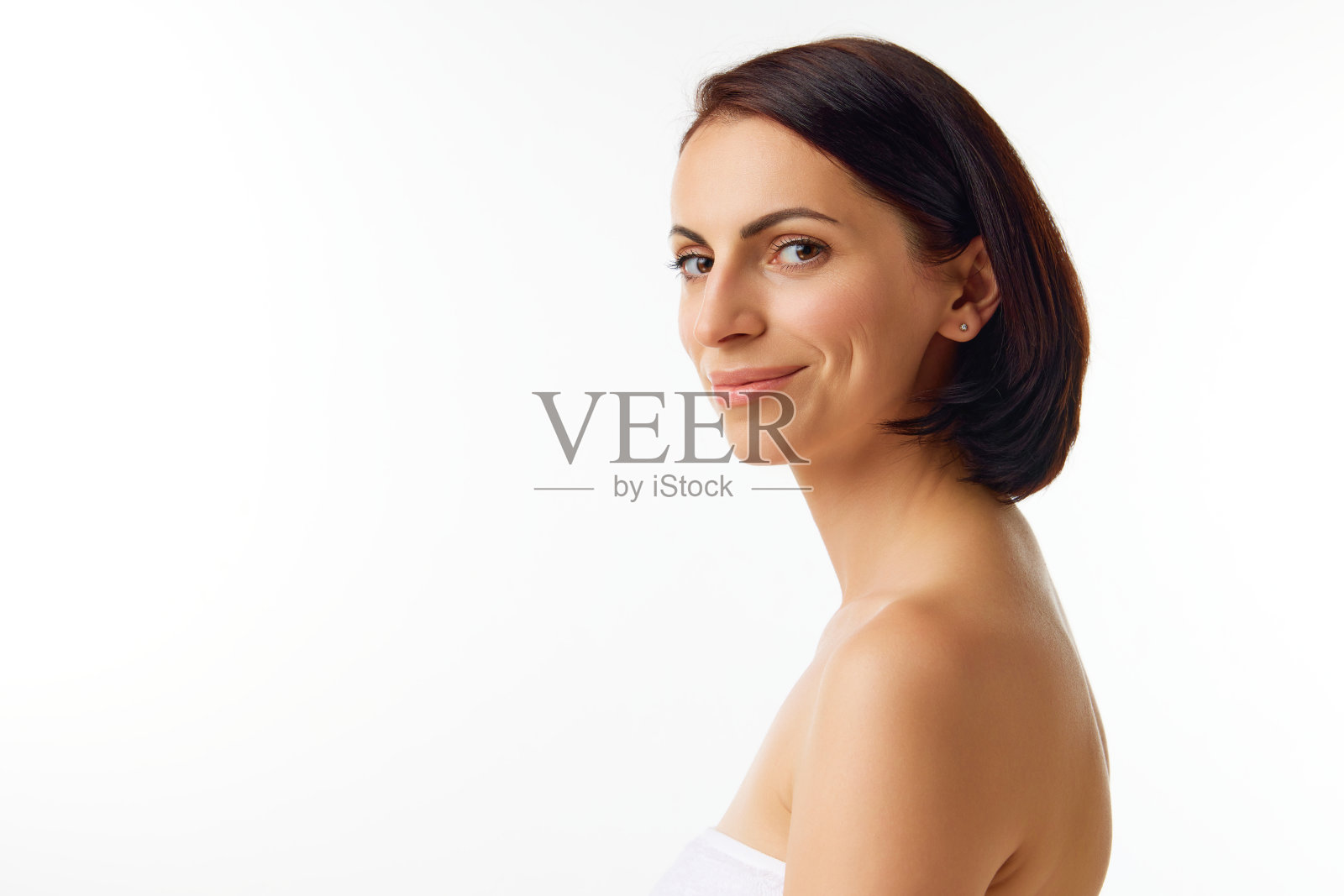 年轻的微笑的女人的侧面肖像，裸露的肩膀和自然的面部化妆看着相机。美颜，干净、清新，肌肤光滑。照片摄影图片