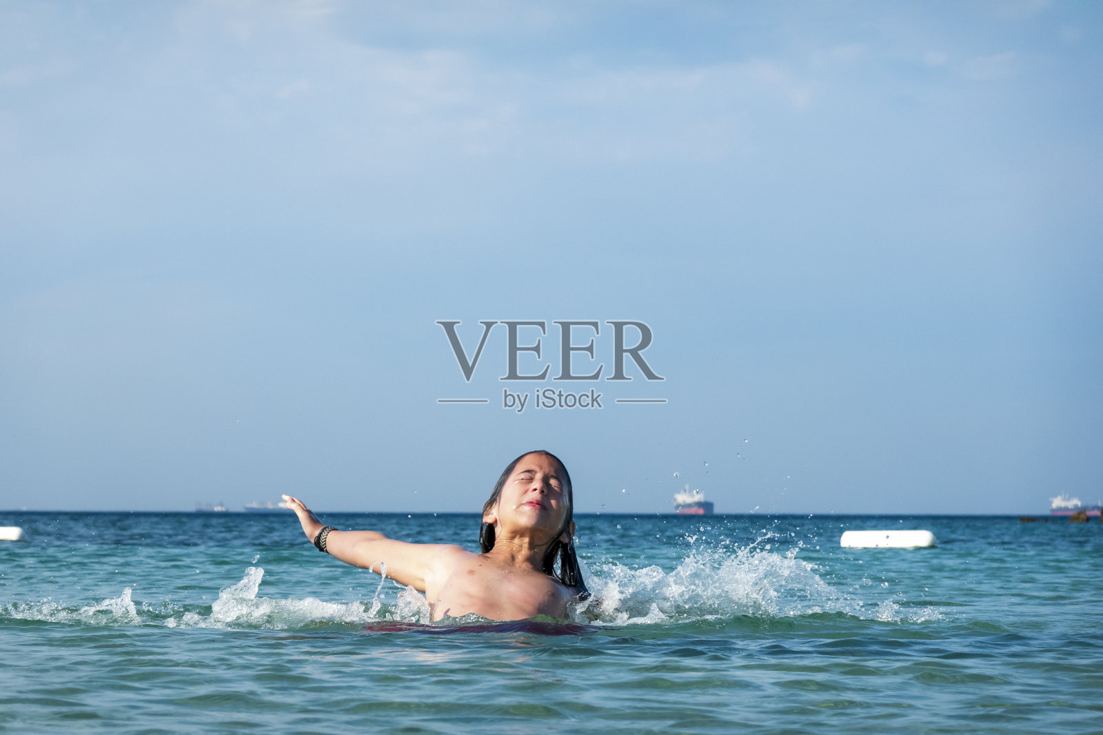 他用手在海里泼水。一个夏天的早晨。忒涅多斯岛。爱琴海北部，12岁的帅哥。长头发的照片摄影图片